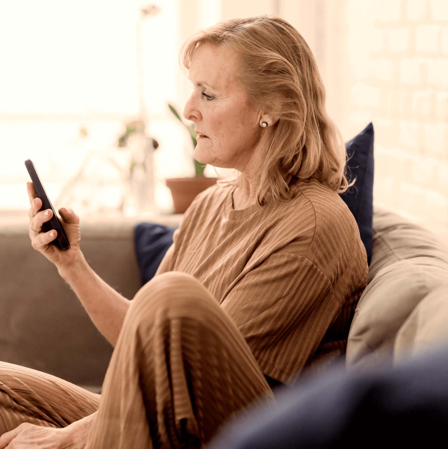A senior woman sitting on a couch, looking at her smartphone.